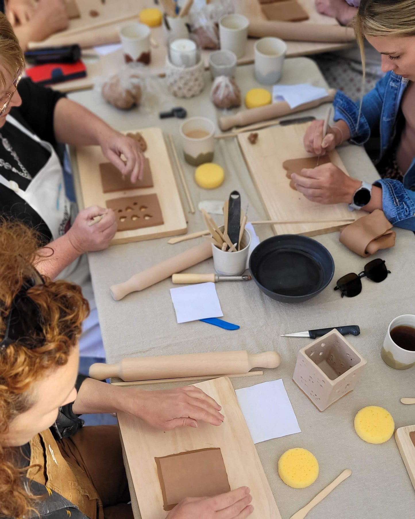 People working with clay and tools on a table in a pottery workshop.