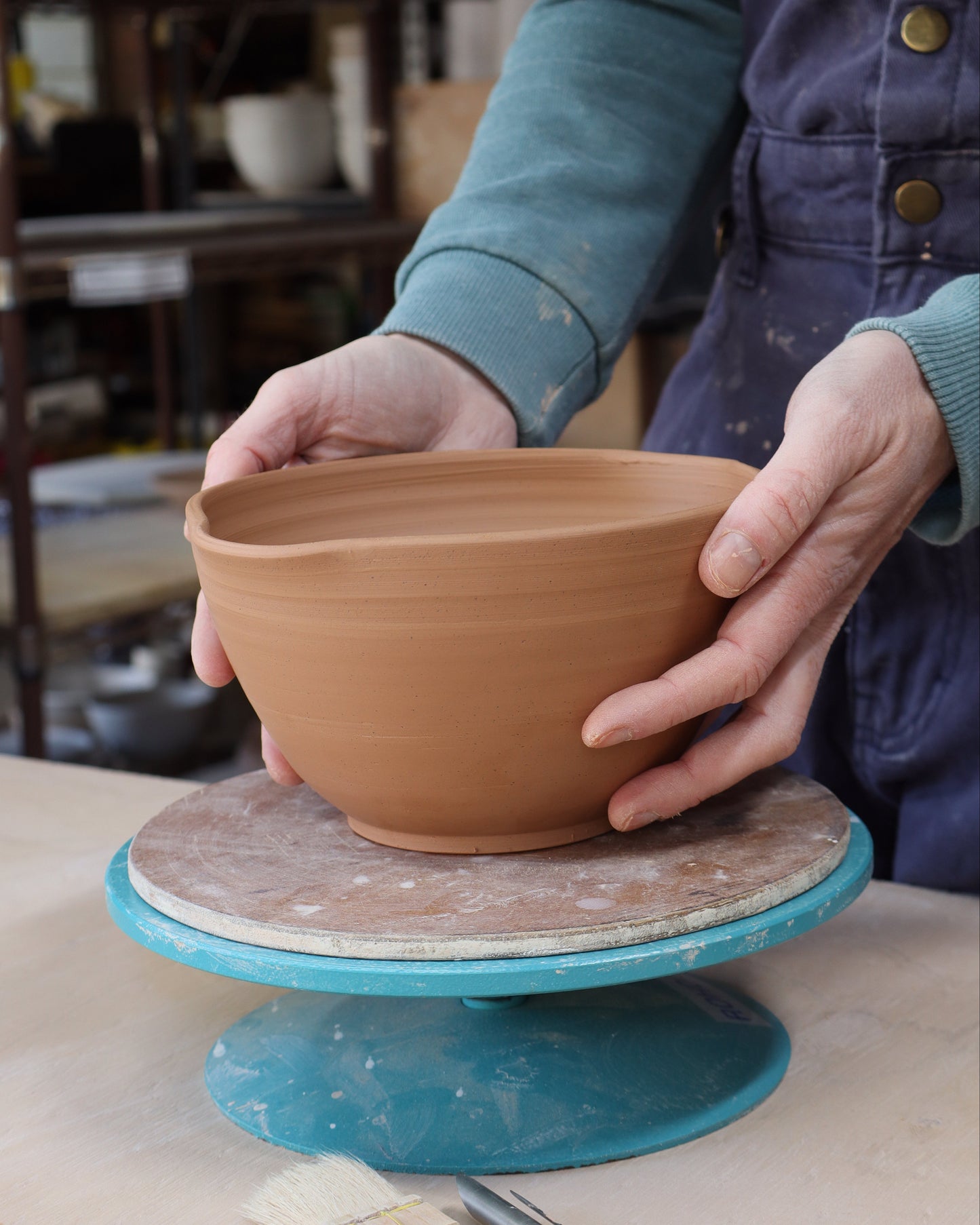 Person holding a ceramic bowl on a banding wheel in a workshop setting