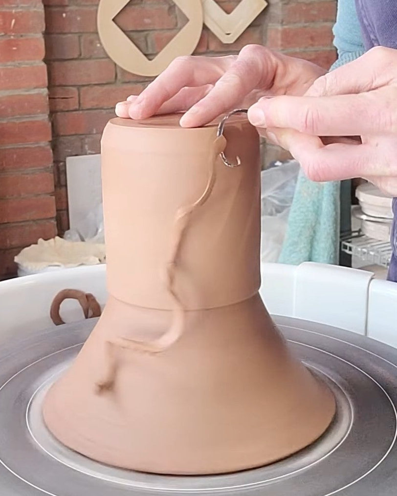Person working on a clay pot on a pottery wheel with a brick wall background