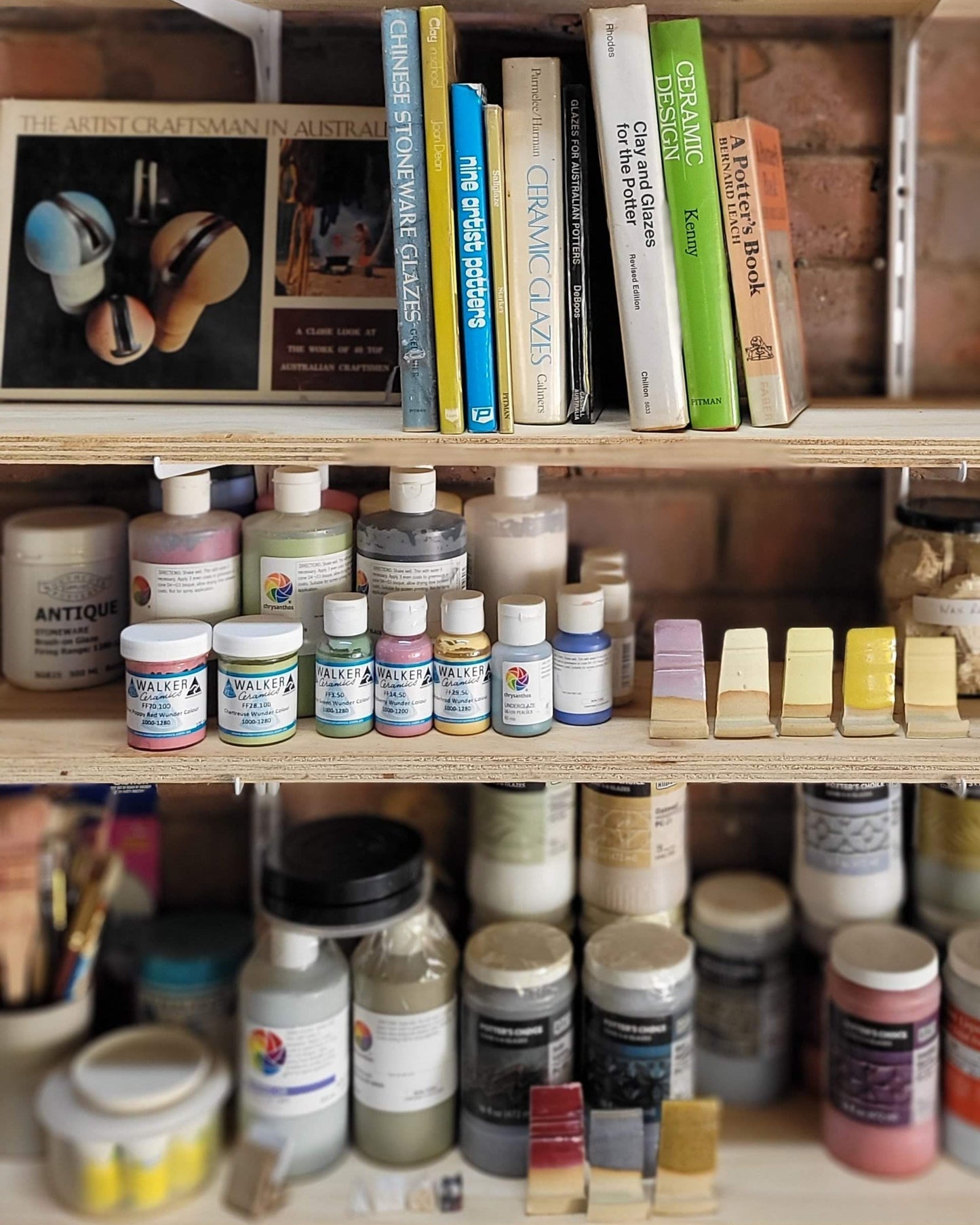 Wooden storage unit with paint bottles and books against a brick wall.