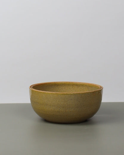 Yellow ceramic bowl leaning against a white wall