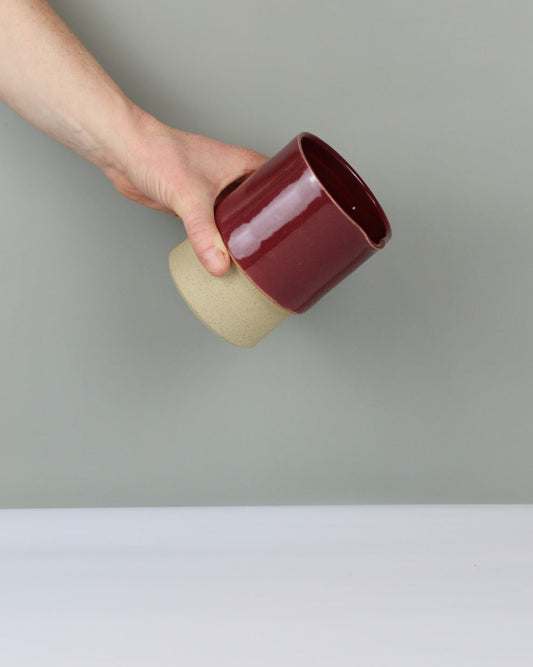 Hand holding a ceramic mug with a deep red glaze against a plain background