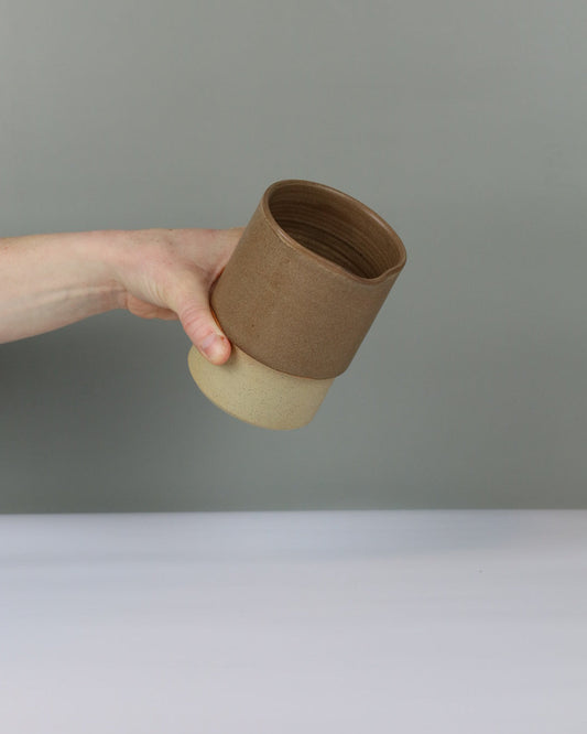 Hand pouring a brown ceramic cup against a plain background