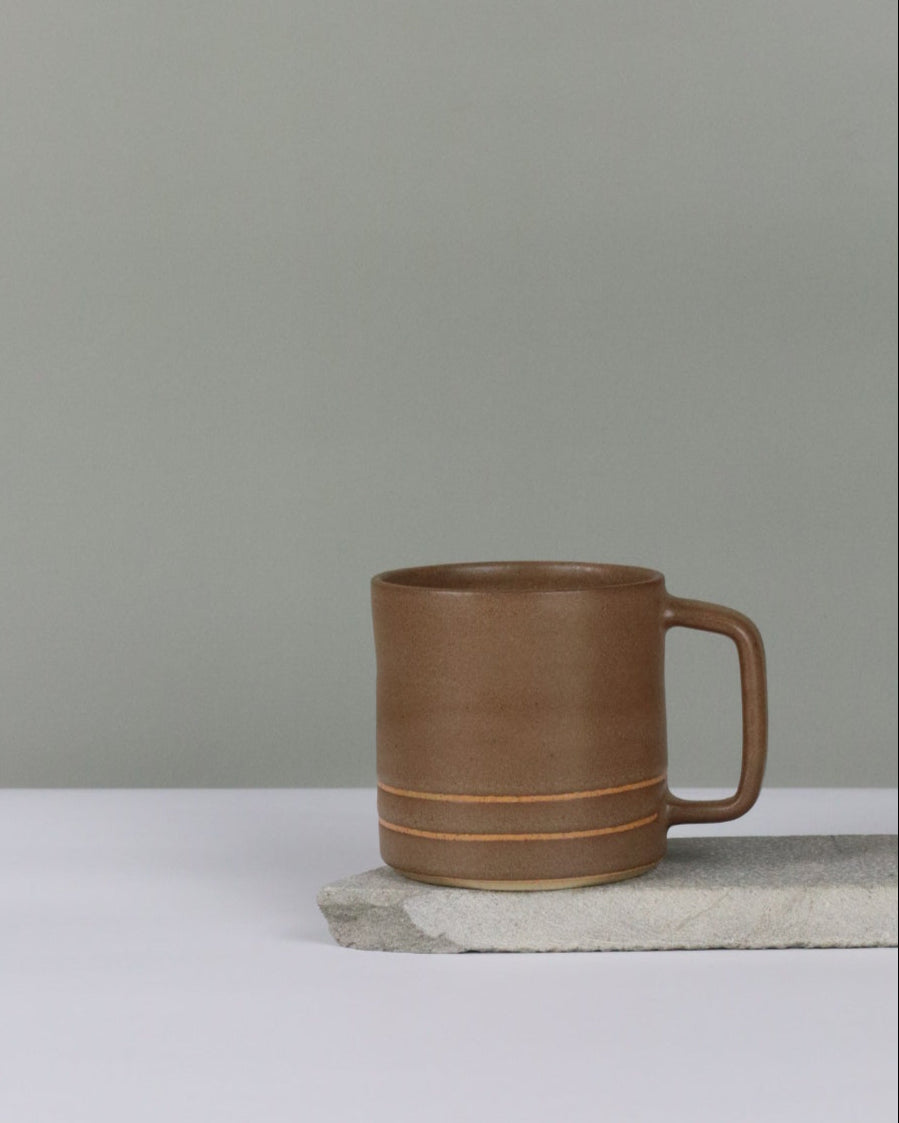 Brown ceramic mug hanging on a grey background.