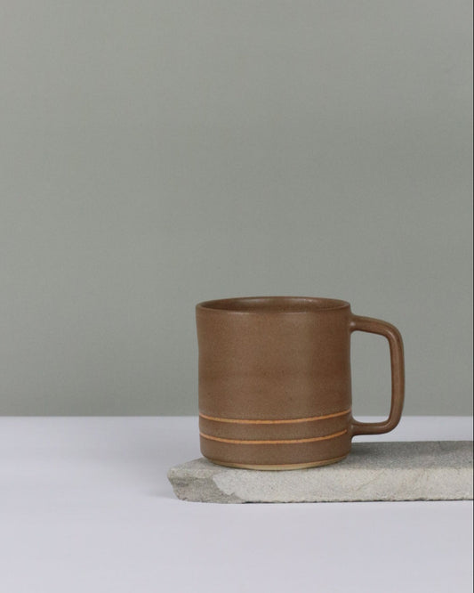 Brown ceramic mug hanging on a grey background.