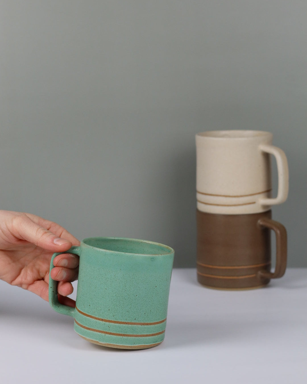 Hand holding a turquoise mug with a plain background