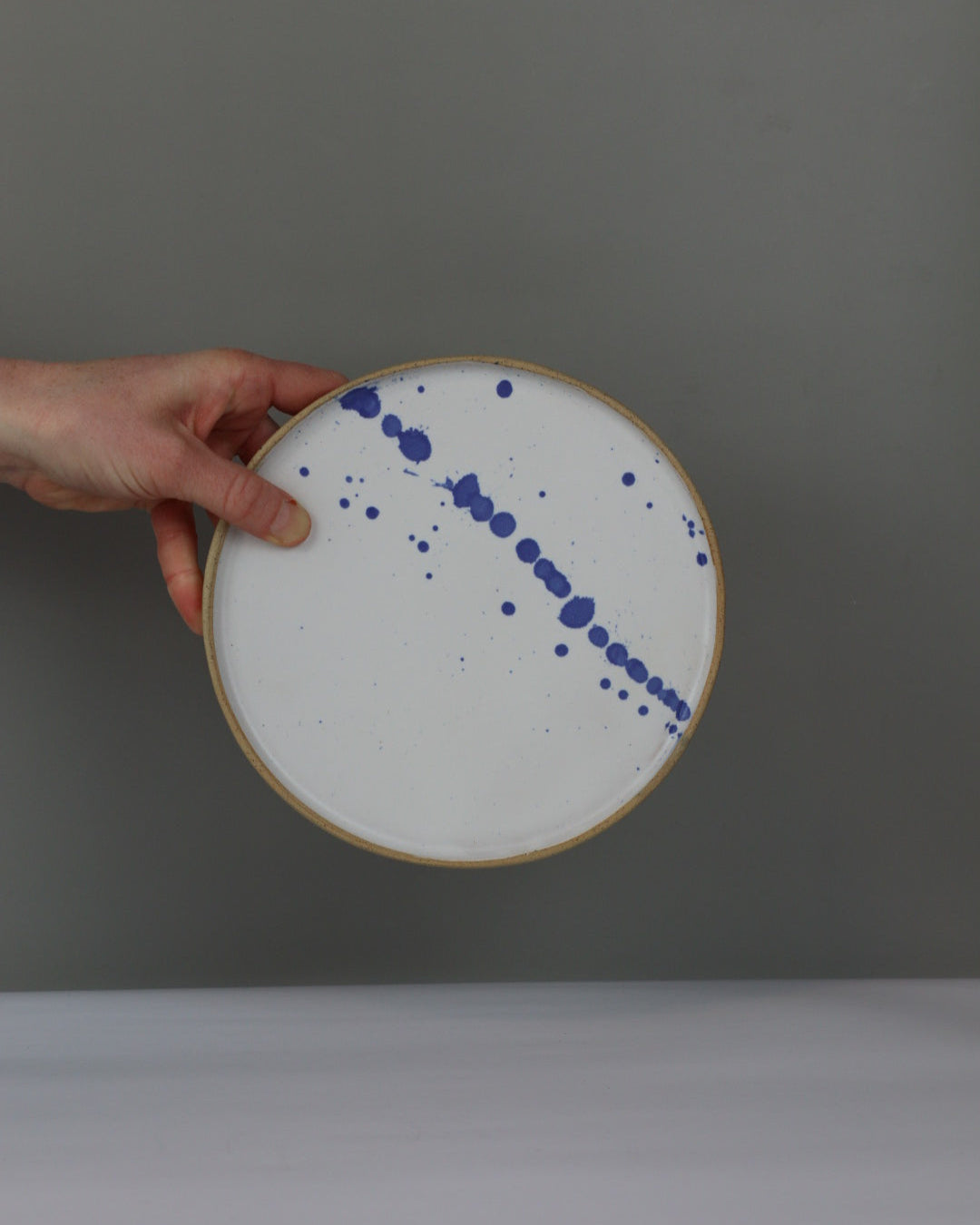 Hand holding a ceramic plate with blue speckles against a gray background