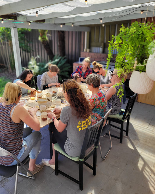 Group of people gathered around a table on a patio working with clay.