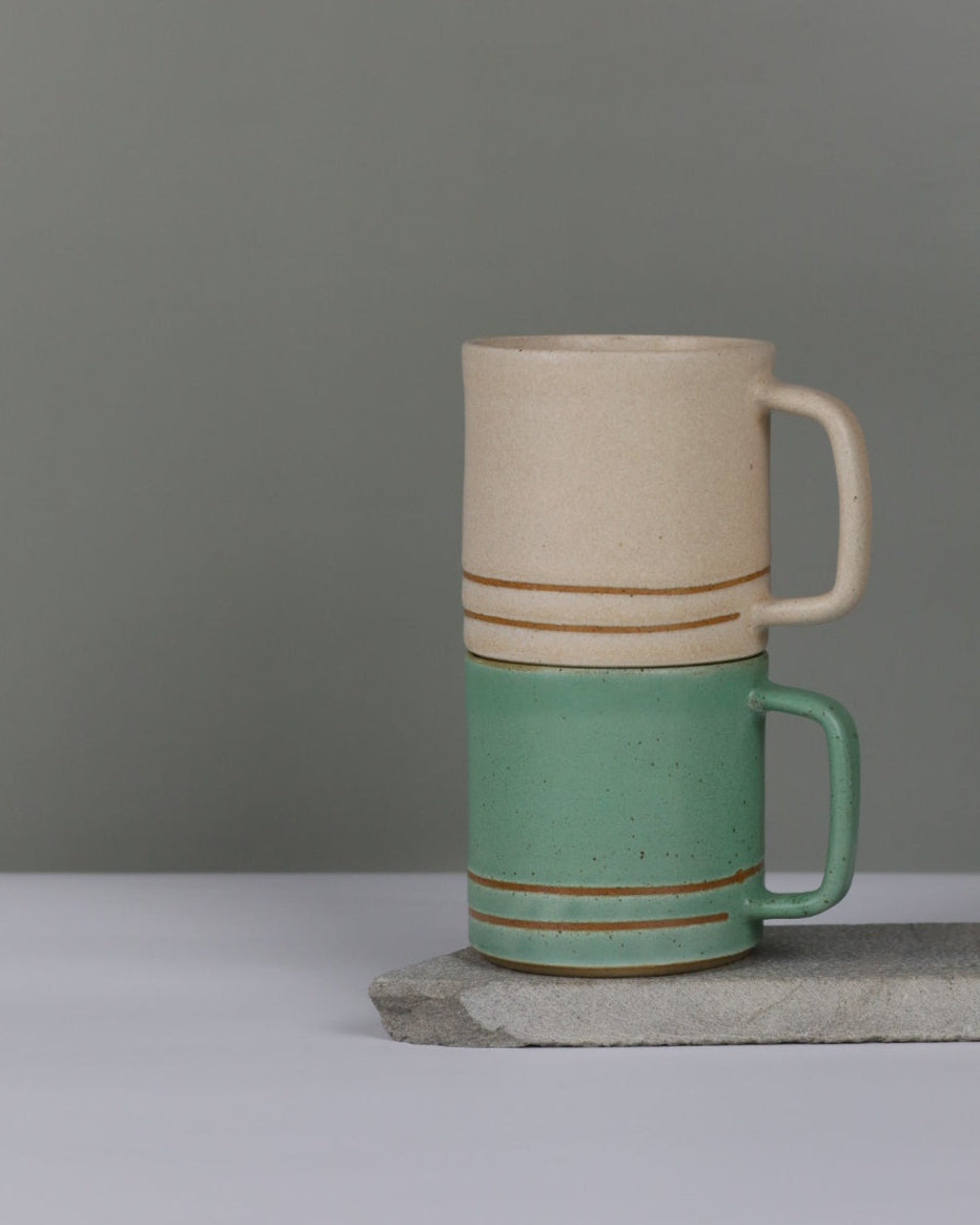 Two ceramic cups with green and oatmeal colours on a grey background