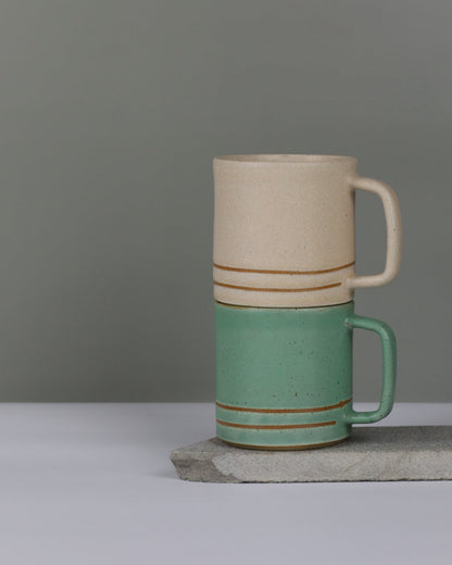Two ceramic cups with green and oatmeal colours on a grey background