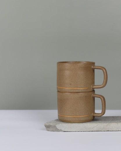 Two brown ceramic mugs stacked on top of eachother against a grey background.