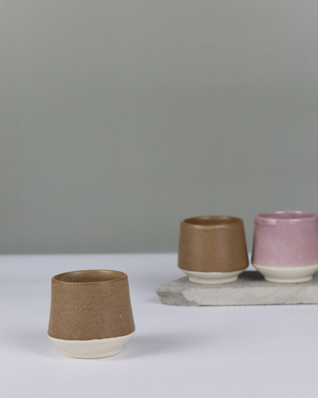 Three small ceramic cups in different colours on a grey background