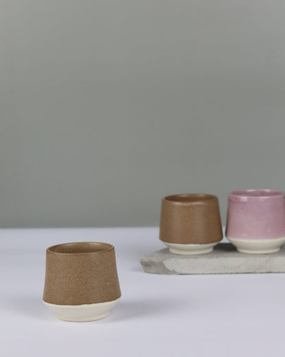 Three small ceramic cups in different colours on a grey background