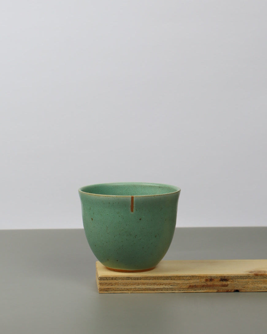 Green ceramic cup on a wooden shelf against a white wall