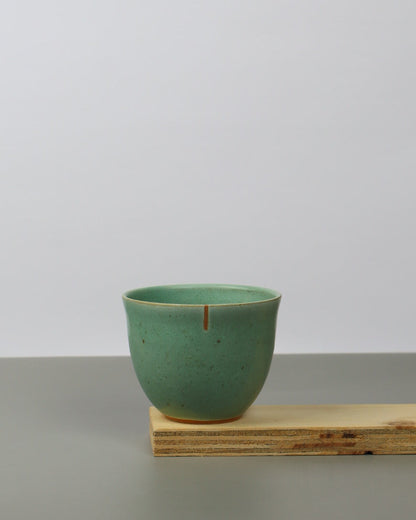 Green ceramic cup on a wooden shelf against a white wall