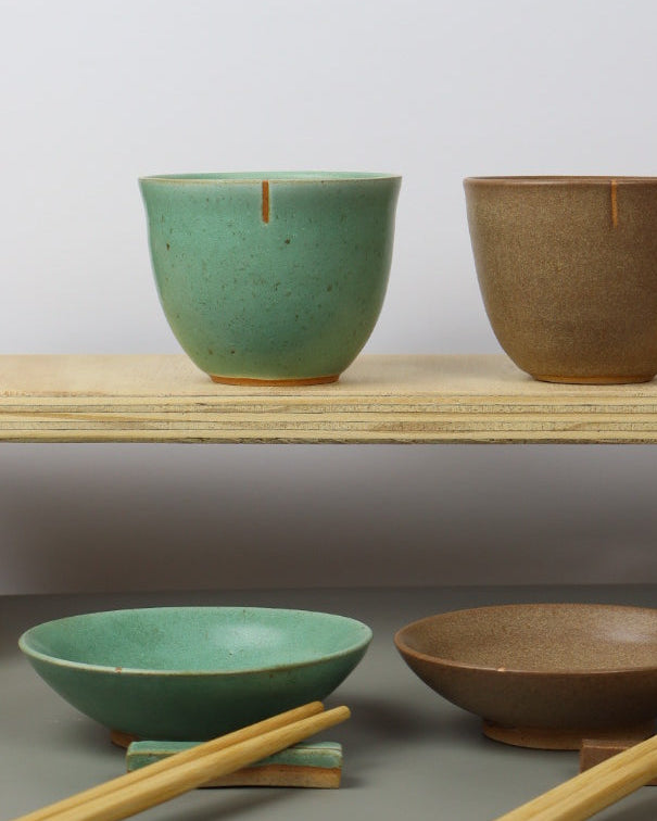 Set of ceramic teacups in various shapes and colors against a gray wall.