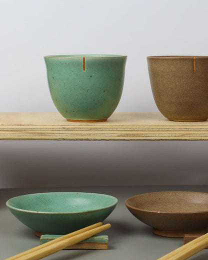 Set of ceramic teacups in various shapes and colors against a gray wall.