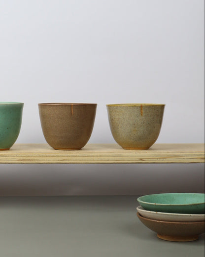 Set of ceramic teacups on a wooden shelf against a light gray background