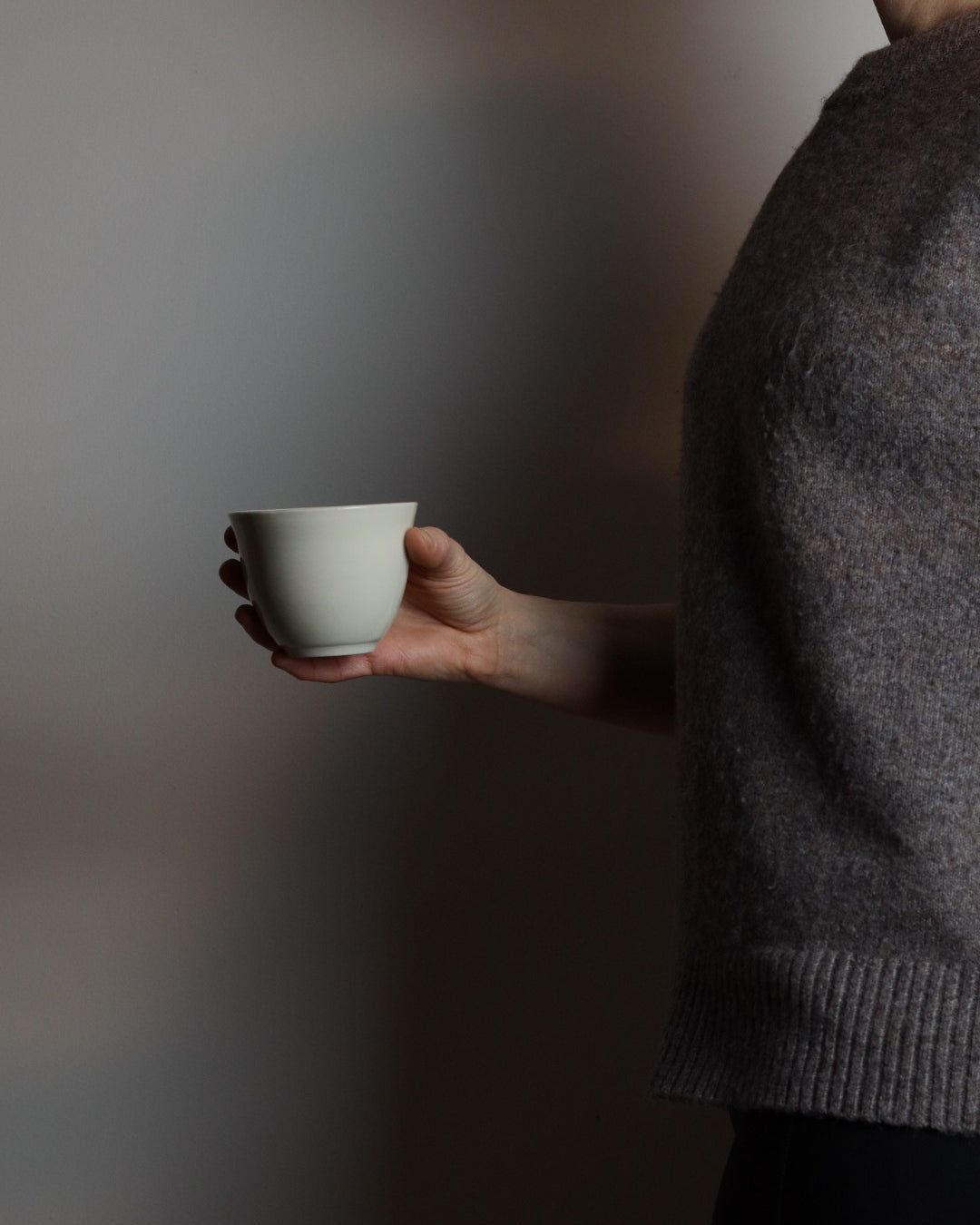 Hand holding a white ceramic teacup against a plain background