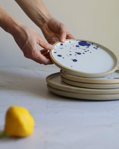 Person holding a ceramic plate with blue speckles against a white wall.