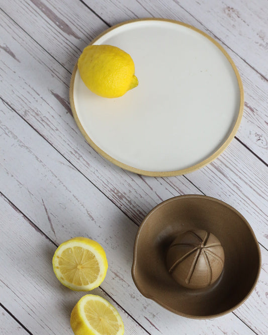 Lemon on a white plate with a brown citrus juicer on a wooden table
