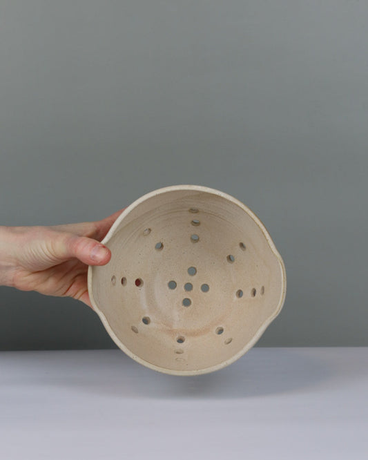 Hand holding a ceramic colander with a plain background
