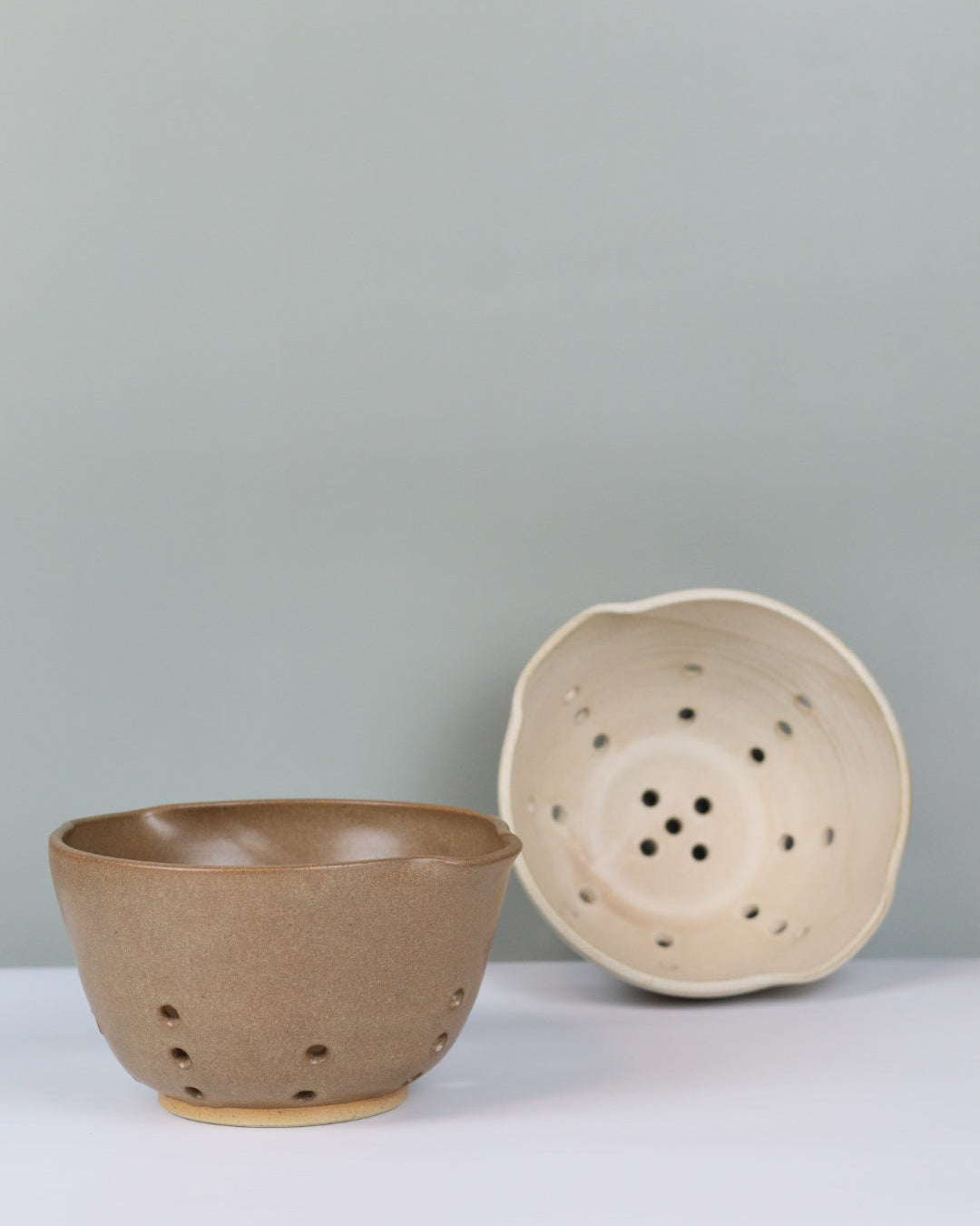 two ceramic colanders against a plain background
