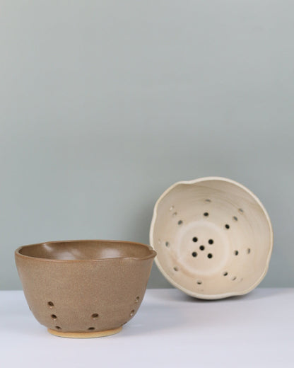 two ceramic colanders against a plain background
