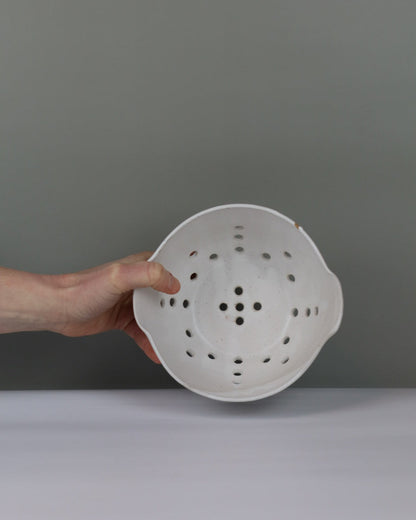 White colander held by a hand against a gray background