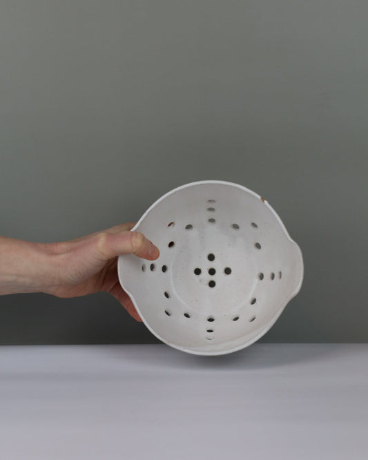 White colander held by a hand against a gray background