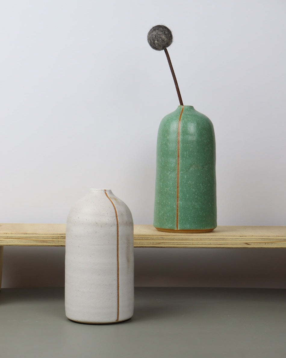 Two ceramicvases, one white and one green, on a wooden stand against a light background.