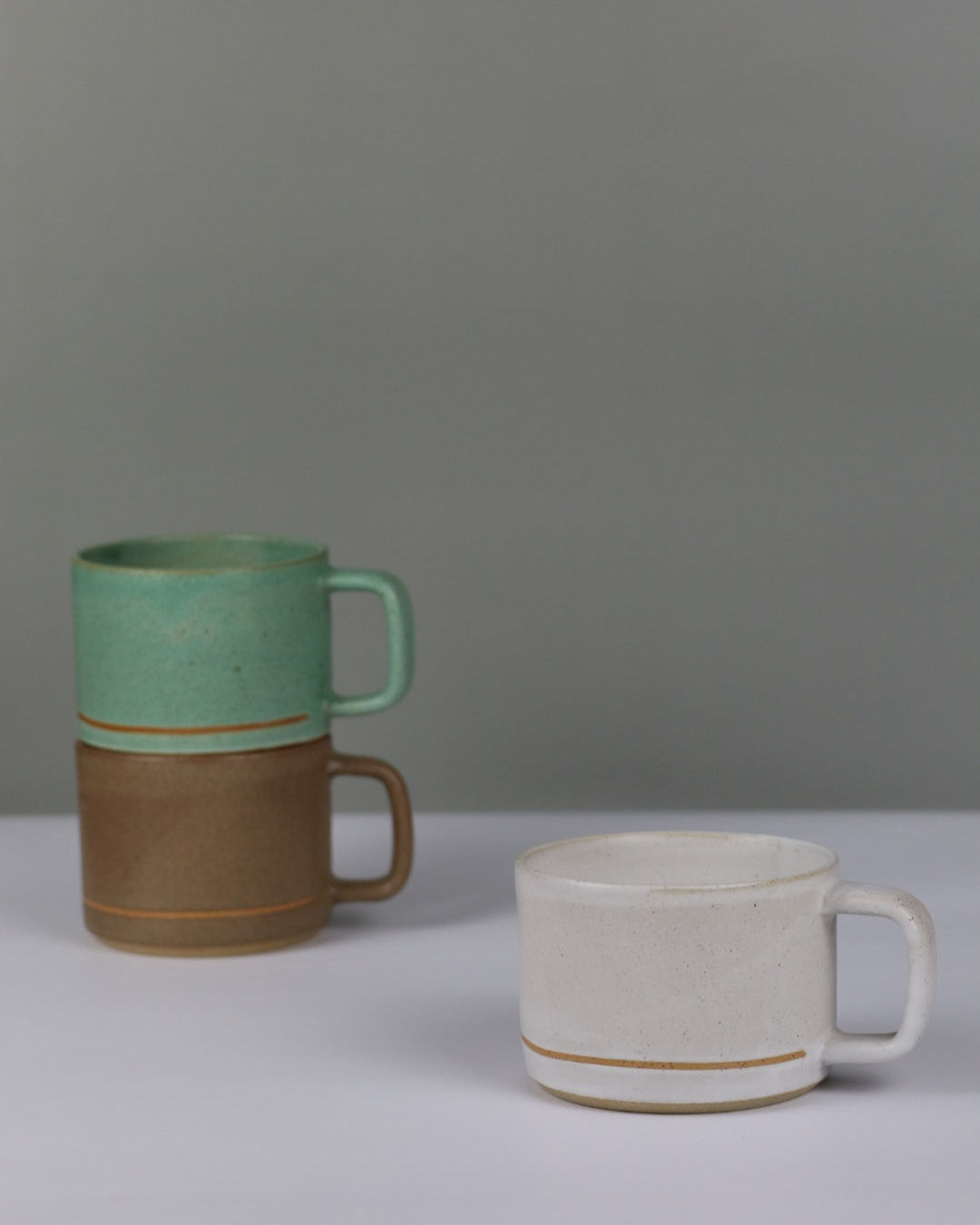 Three ceramic mugs of different colors on a grey wall.
