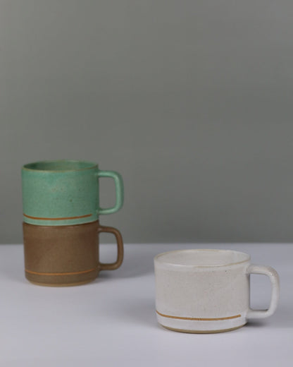 Three ceramic mugs of different colors on a grey wall.