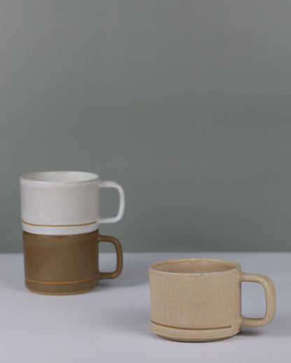 Three ceramic mugs in beige, brown, and white on a grey background.