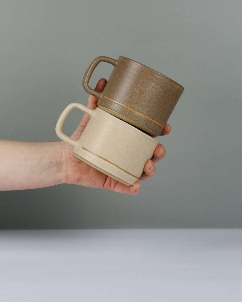 Hand holding two ceramic mugs against a neutral background