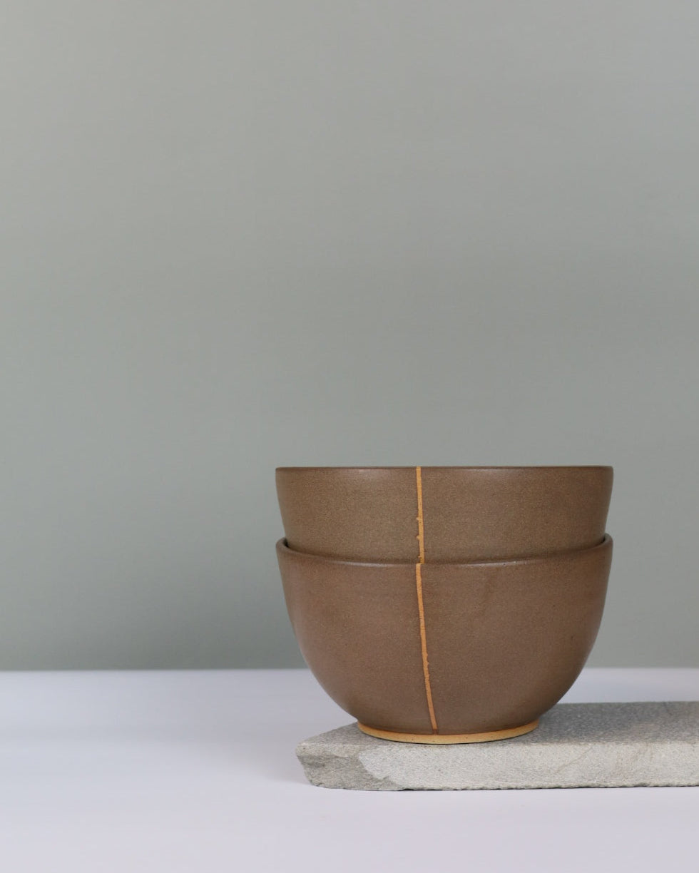 stack of two ceramic bowls in dark brown on a grey background