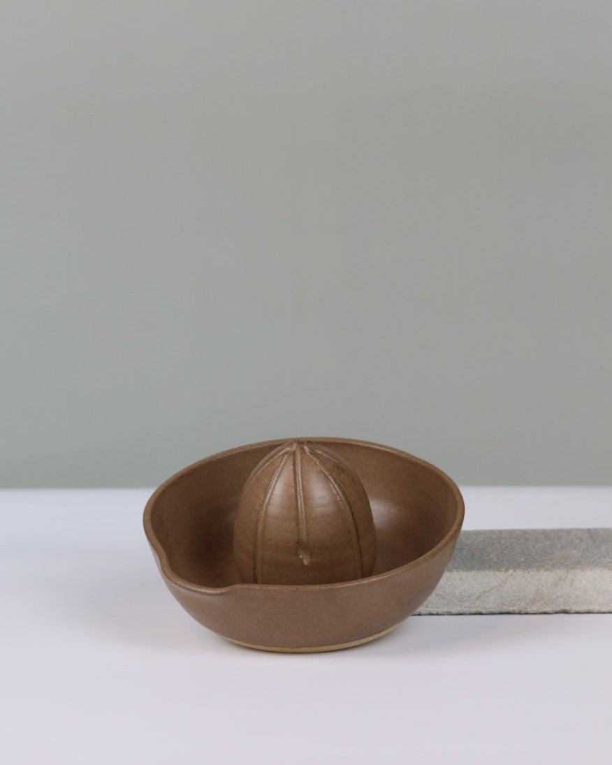 brown ceramic citrus juicer propped up to show the inside on a grey background