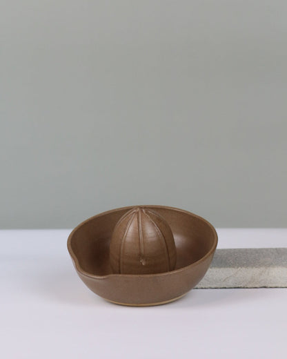 brown ceramic citrus juicer propped up to show the inside on a grey background