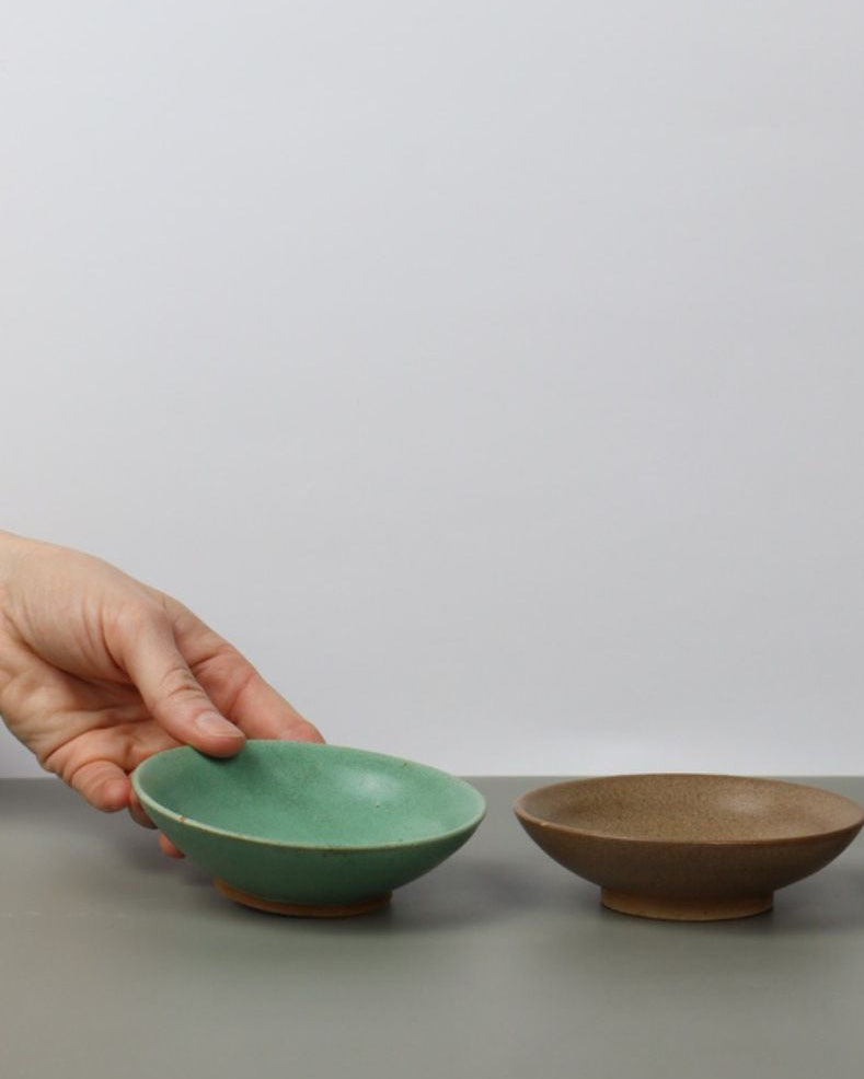Three ceramic bowls in green, brown, and beige on a gray surface with a white background