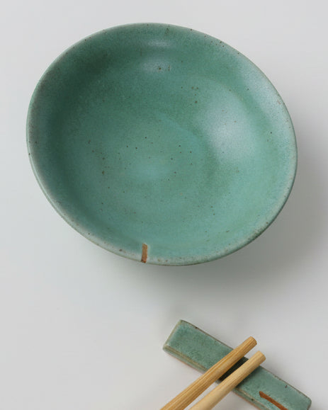 Green ceramic bowl with chopsticks on a gray background