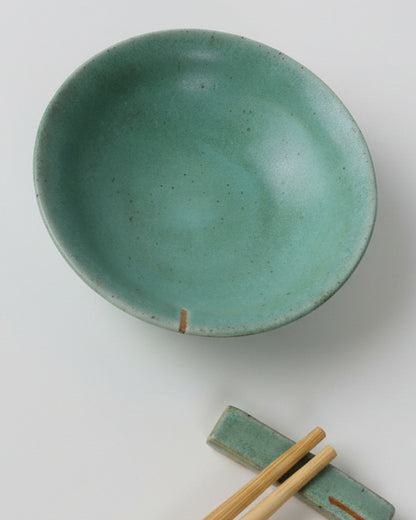 Green ceramic bowl with chopsticks on a gray background