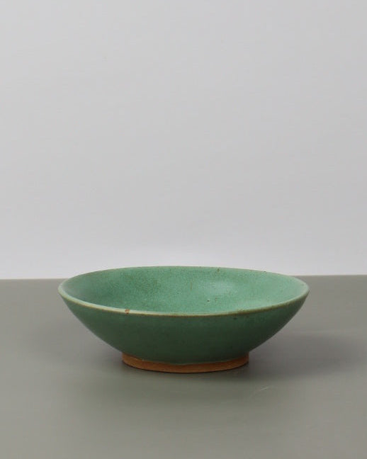 Green ceramic cup leaning against a white wall
