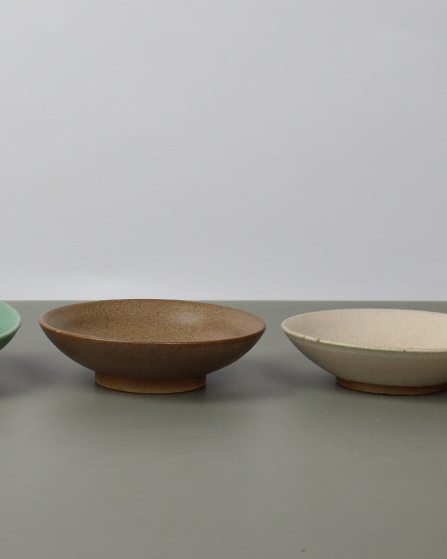 Hand holding a green ceramic bowl against a plain white wall with two other bowls attached.