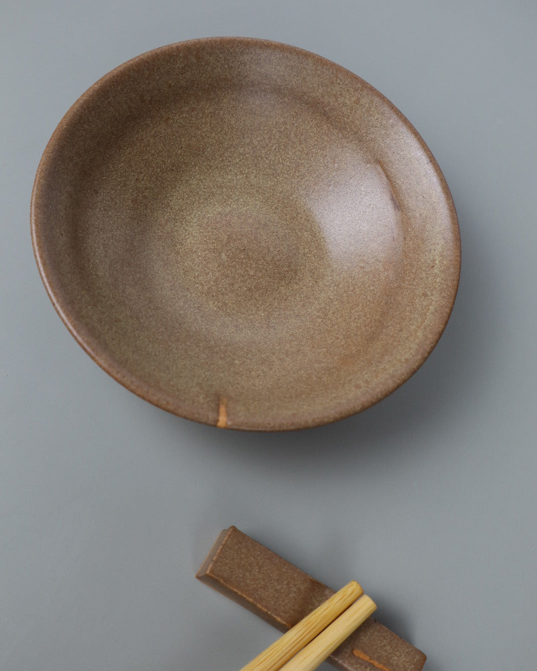 Brown ceramic bowl with chopsticks on a gray background