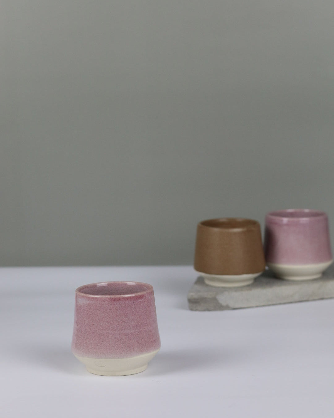 three small ceramic tumblers in pink and brown on a grey background