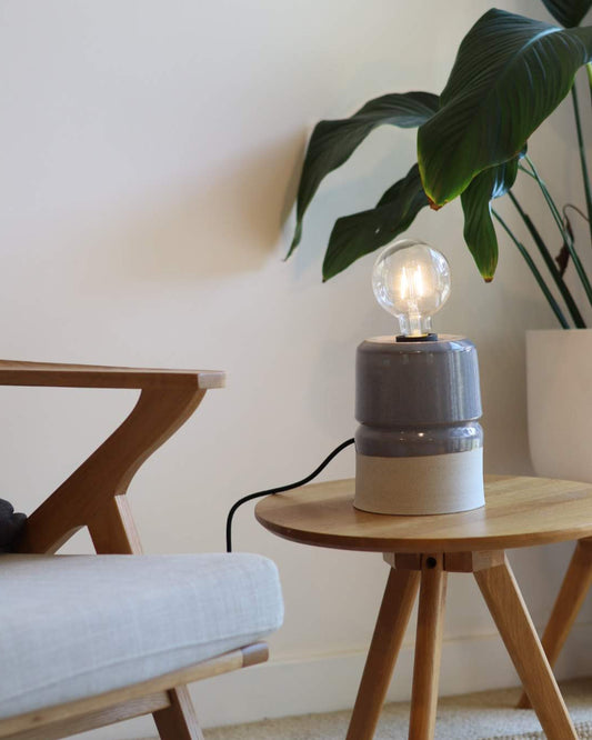 Small lamp with a visible light bulb on a white surface next to a plant