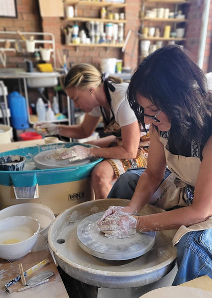 Two people working with pottery on a wheel in a workshop.