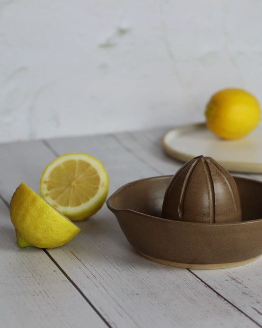 Brown ceramic lemon squeezer with lemons on a wooden surface