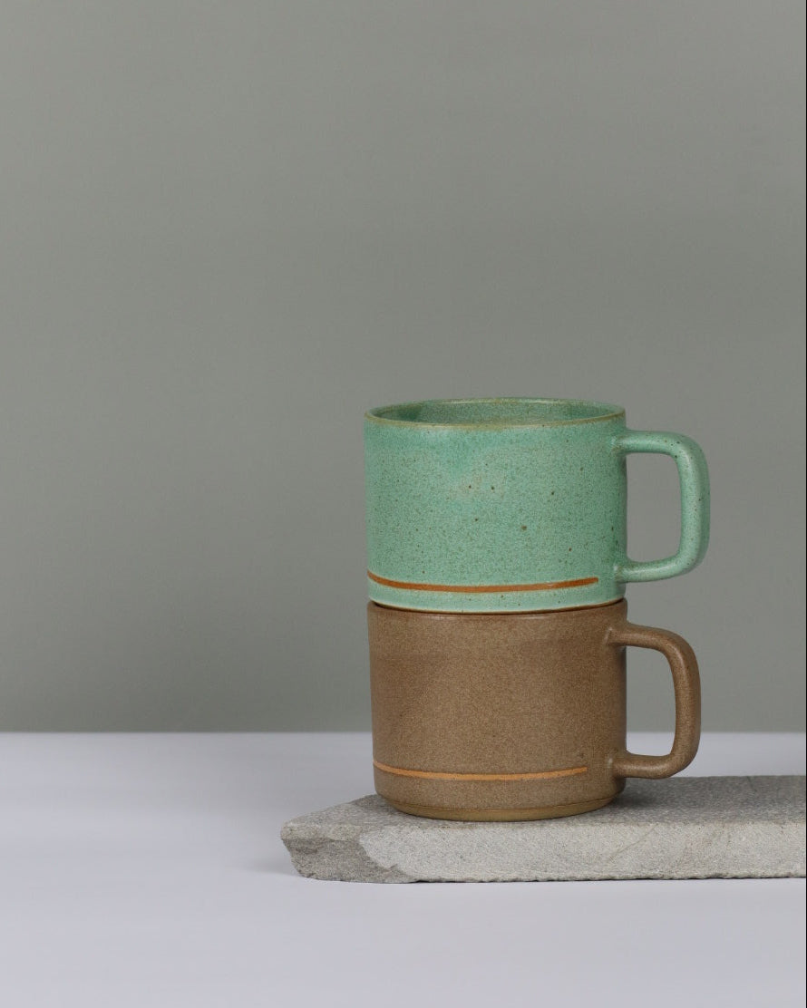 Two ceramic mugs, one brown and one green, stacked on top of each other.