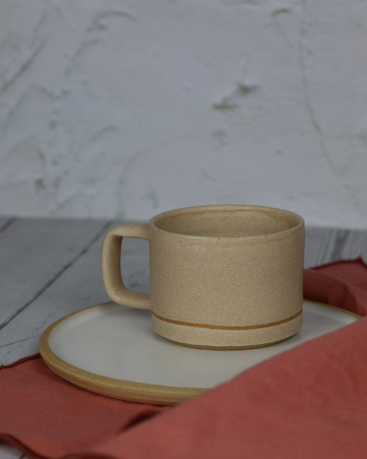 beige ceramic mug on top of a white plate with a pink napkin in the foreground